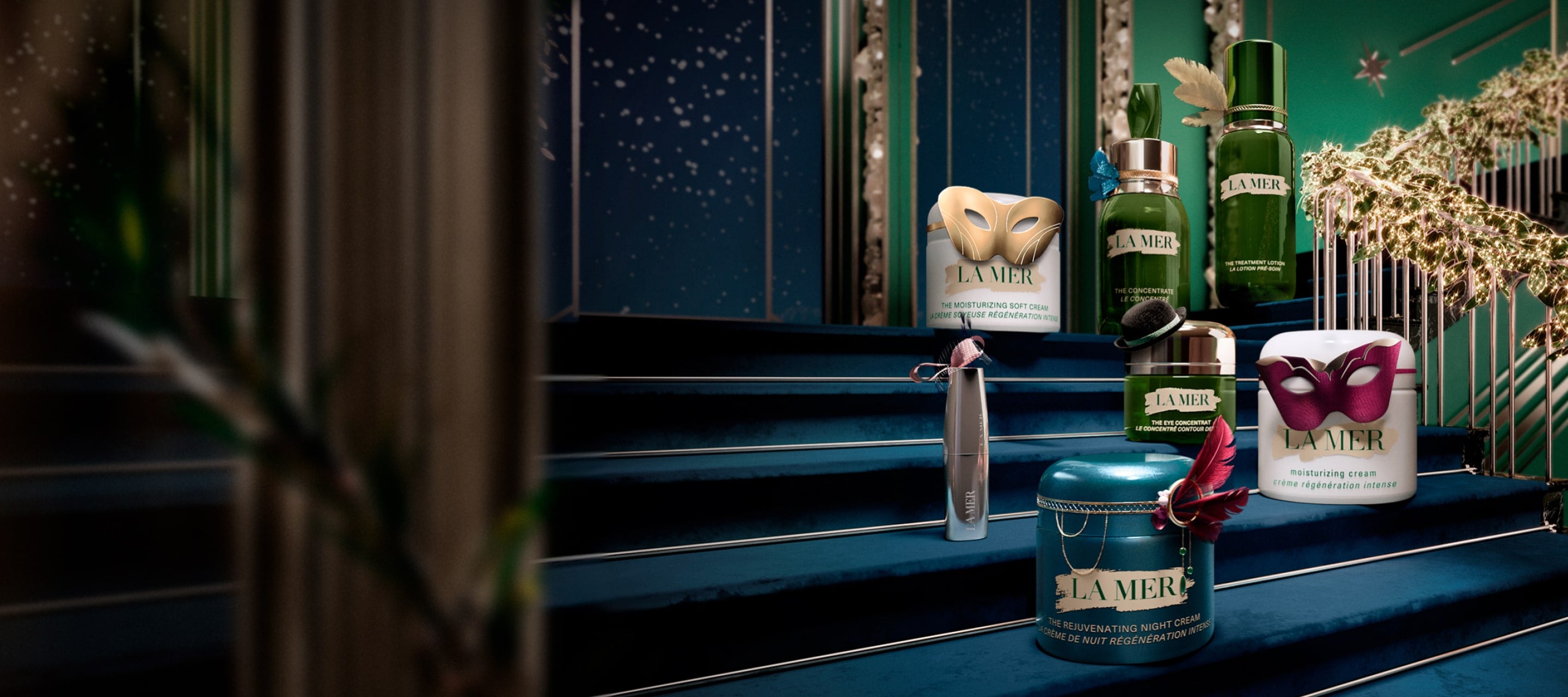 Selection of bestselling La Mer products placed on a festive, grand staircase, decorated in miniature masquerades and headwear